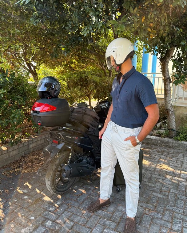 Denisi Murataj in a helmet, beside a scooter loaded up for a trip.